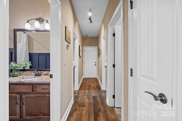 hallway featuring dark wood-style flooring, baseboards, and a sink