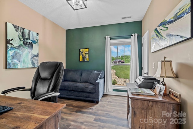 office area with a textured ceiling, wood finished floors, and visible vents
