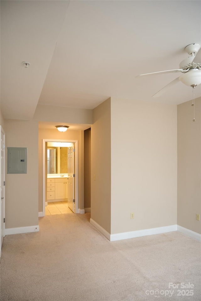 unfurnished room with light colored carpet, a ceiling fan, baseboards, and electric panel