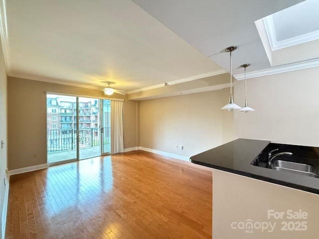 unfurnished living room with baseboards, a skylight, ornamental molding, and light wood-type flooring