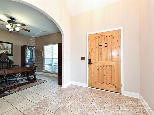 entryway featuring ceiling fan, arched walkways, baseboards, a towering ceiling, and visible vents