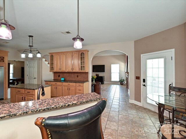 kitchen featuring visible vents, arched walkways, tasteful backsplash, glass insert cabinets, and light brown cabinets