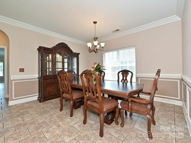 dining area featuring an inviting chandelier, ornamental molding, wainscoting, and arched walkways
