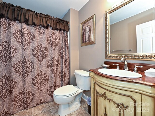bathroom with curtained shower, vanity, tile patterned floors, baseboards, and toilet