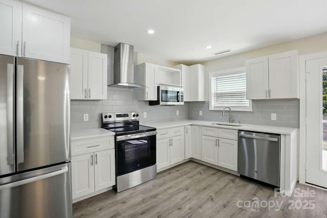 kitchen with light countertops, stainless steel appliances, a sink, and wall chimney exhaust hood