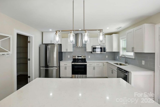 kitchen with wall chimney range hood, decorative backsplash, a sink, white cabinets, and stainless steel appliances