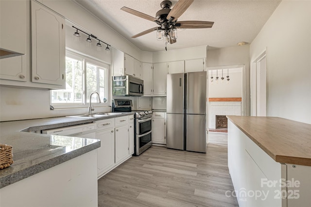 kitchen with ceiling fan, a sink, light wood-style floors, a textured ceiling, and stainless steel appliances