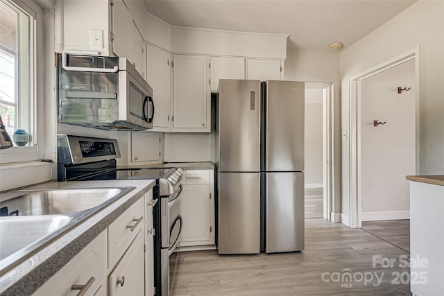 kitchen featuring light wood finished floors, light countertops, stainless steel appliances, baseboards, and white cabinetry
