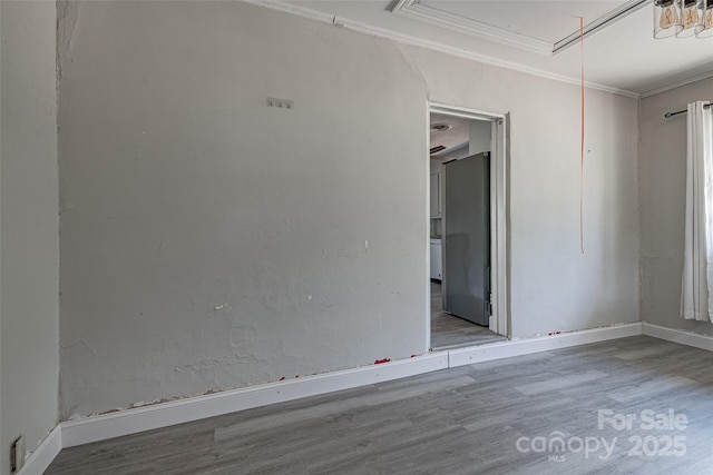 empty room featuring crown molding, baseboards, wood finished floors, and attic access