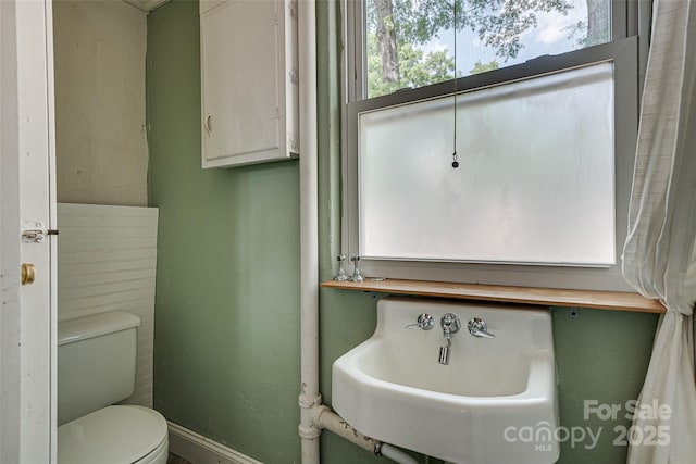 half bathroom with a sink, baseboards, and toilet