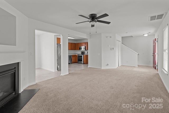 unfurnished living room with light colored carpet, a glass covered fireplace, ceiling fan, and baseboards