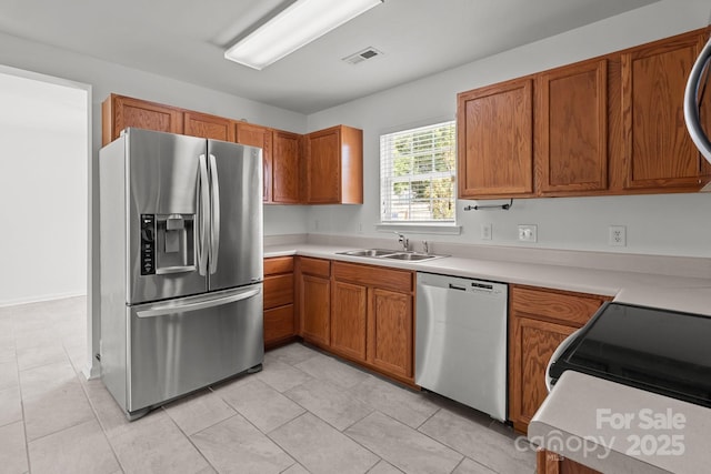 kitchen with stainless steel appliances, a sink, brown cabinetry, and light countertops