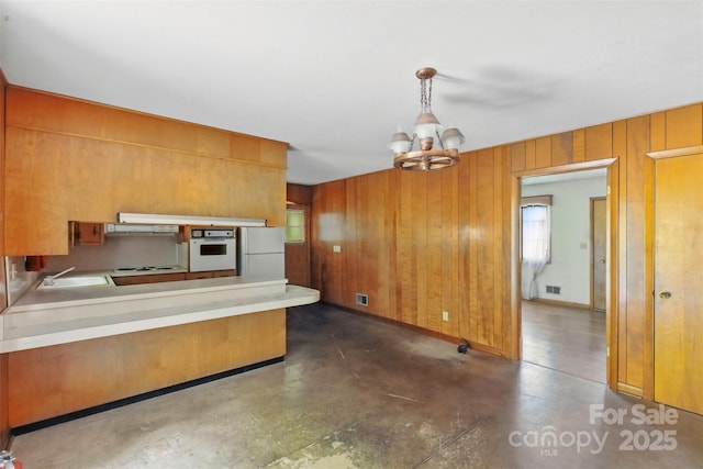 3120 Mineral Springs Mountain Rd, Valdese, NC 28690 - kitchen with white appliances, under cabinet range hood, wooden walls, brown cabinetry, and a chandelier