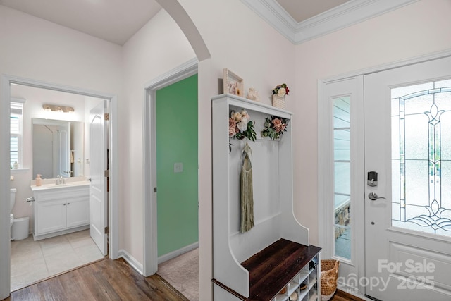 entryway with arched walkways, ornamental molding, baseboards, and light wood-style flooring