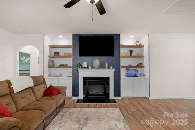 living room featuring a ceiling fan, visible vents, a fireplace with flush hearth, arched walkways, and light wood-style flooring