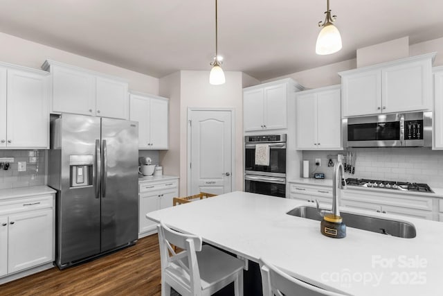 kitchen with pendant lighting, white cabinetry, a sink, backsplash, and stainless steel appliances
