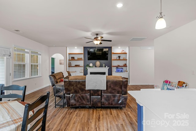 living room featuring arched walkways, light wood-style flooring, a ceiling fan, baseboards, and visible vents