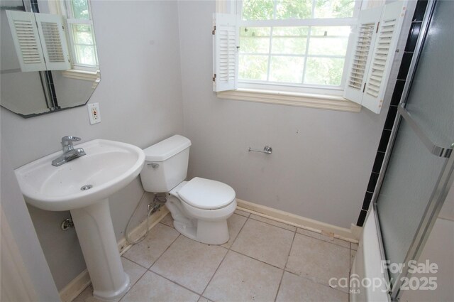 bathroom with a shower with shower door, a sink, tile patterned floors, baseboards, and toilet