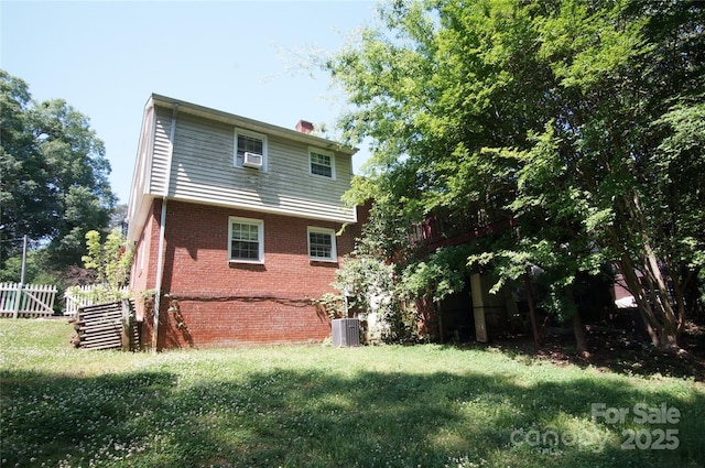 rear view of house with fence, cooling unit, a chimney, brick siding, and a lawn