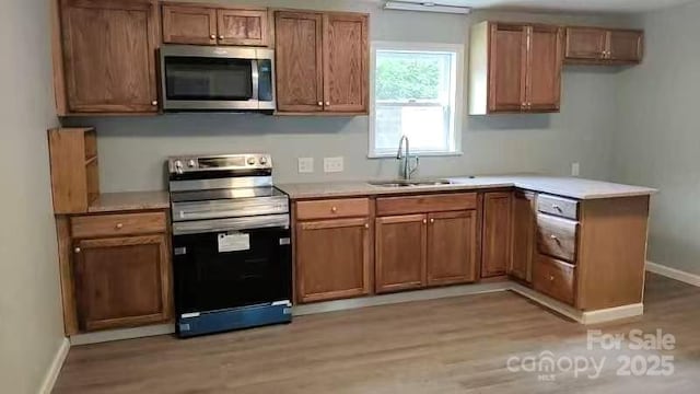 kitchen with a sink, light countertops, stainless steel appliances, and light wood-type flooring