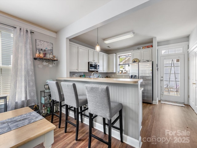 6909 Dunton St, Huntersville, NC 28078 - kitchen with appliances with stainless steel finishes, a peninsula, decorative light fixtures, wood finished floors, and a kitchen bar