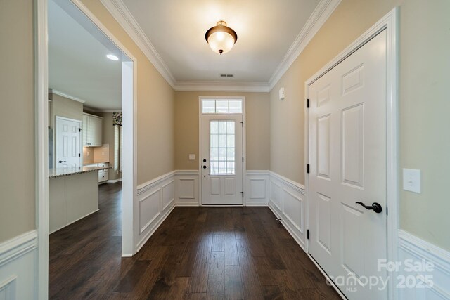 doorway with crown molding, wainscoting, dark wood-type flooring, and visible vents
