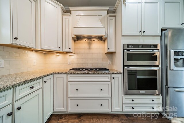 kitchen featuring custom range hood, decorative backsplash, light stone countertops, and stainless steel appliances
