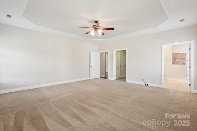 spare room featuring ceiling fan, light carpet, baseboards, a tray ceiling, and visible vents