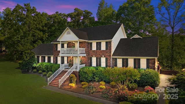 view of front of house featuring a shingled roof, brick siding, a front lawn, and a balcony