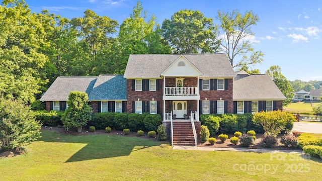 georgian-style home featuring brick siding, a shingled roof, a balcony, and a front lawn