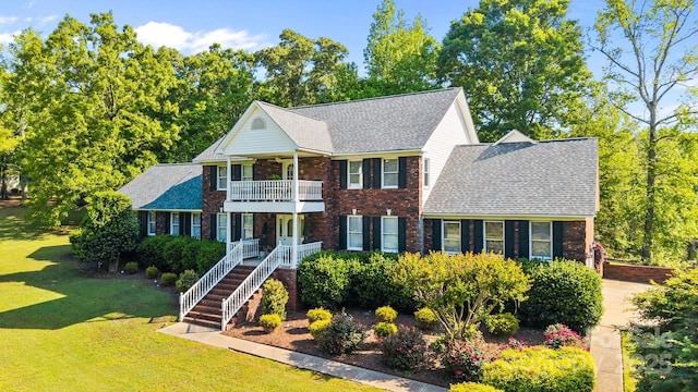view of front of property with brick siding, a shingled roof, a balcony, and a front yard