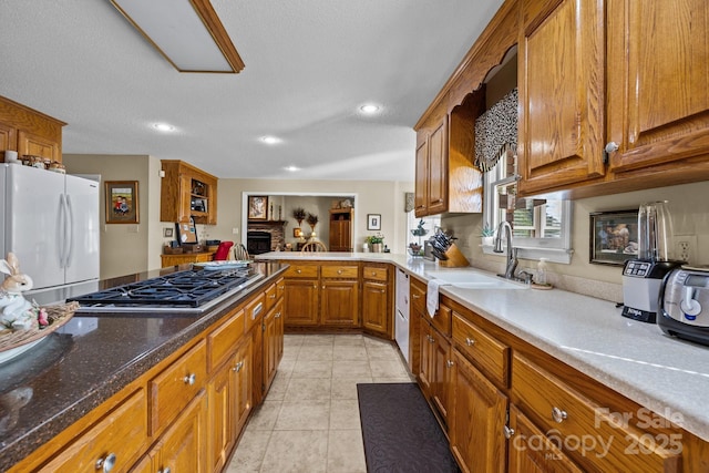 kitchen featuring brown cabinetry, a sink, freestanding refrigerator, stainless steel gas stovetop, and recessed lighting