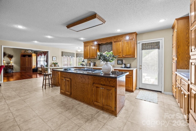 kitchen with a center island, a textured ceiling, stainless steel gas cooktop, and brown cabinets