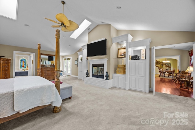 carpeted bedroom featuring baseboards, a glass covered fireplace, a skylight, and high vaulted ceiling