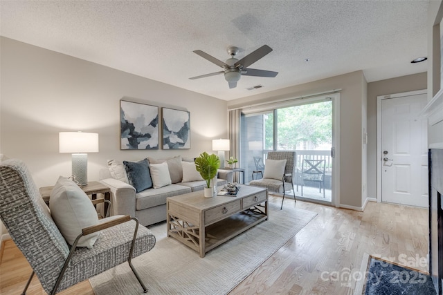 living room with a textured ceiling, ceiling fan, light wood-style floors, and baseboards