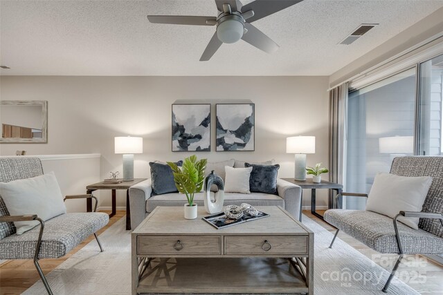 living area with light wood-style flooring, a ceiling fan, and a textured ceiling