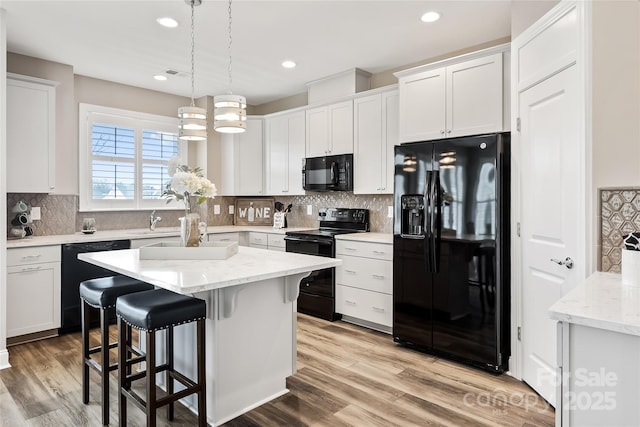 kitchen featuring white cabinets, black appliances, light wood-style floors, a breakfast bar, and recessed lighting