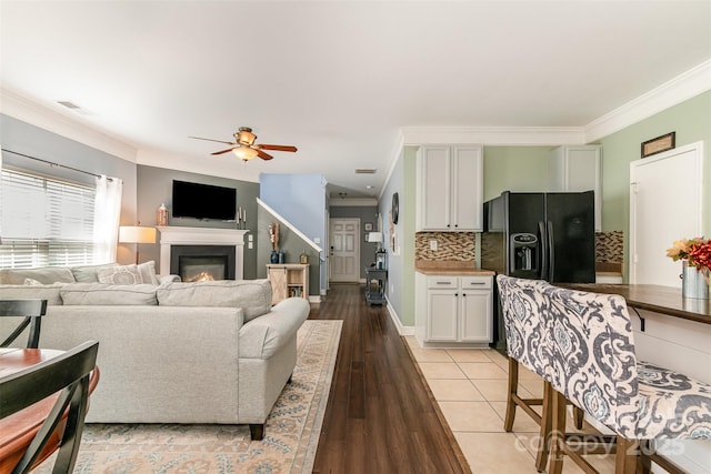 living area featuring crown molding, visible vents, a lit fireplace, a ceiling fan, and light wood finished floors
