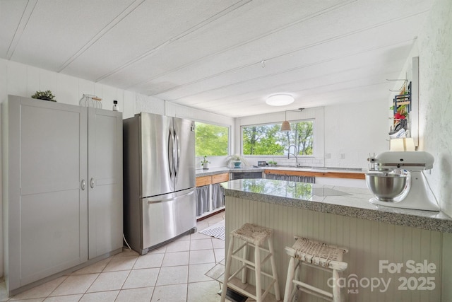 kitchen with freestanding refrigerator, a peninsula, light tile patterned flooring, a breakfast bar area, and a sink