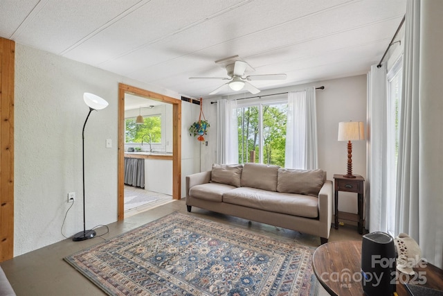 living area with a textured ceiling, ceiling fan, a textured wall, and a wealth of natural light