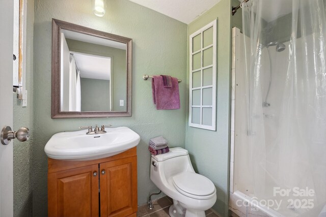 full bath featuring vanity, a textured wall, a shower stall, and toilet