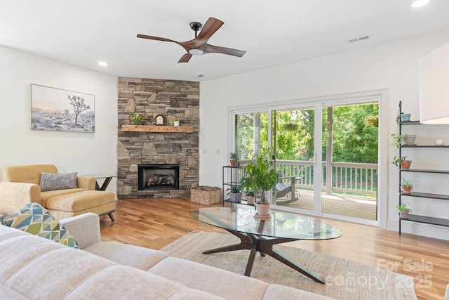 living room featuring a ceiling fan, a stone fireplace, visible vents, wood finished floors, and recessed lighting