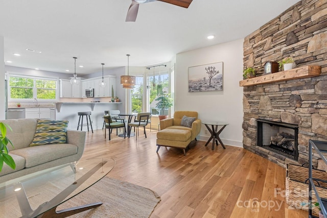 living area featuring recessed lighting, a ceiling fan, light wood finished floors, and a stone fireplace