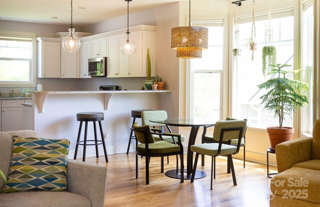 kitchen with white cabinets, a breakfast bar area, light wood-style flooring, stainless steel microwave, and decorative light fixtures