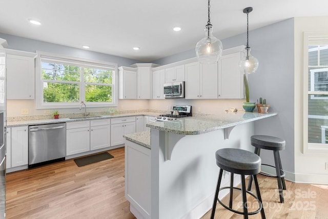 kitchen featuring white cabinets, stainless steel appliances, a sink, and light wood-style flooring
