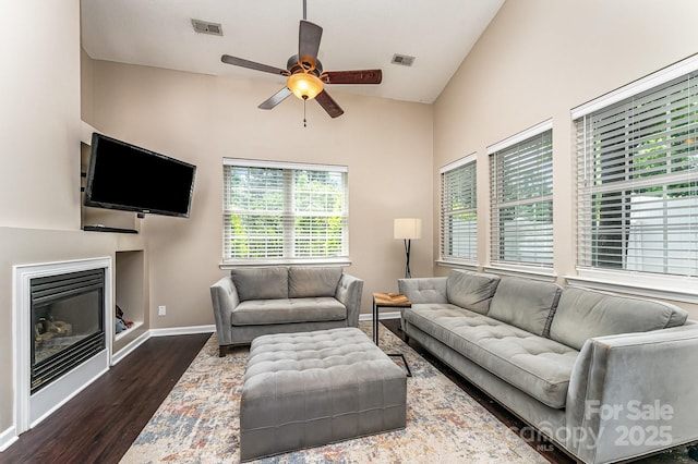 living room with visible vents, vaulted ceiling, ceiling fan, dark wood-style flooring, and a glass covered fireplace