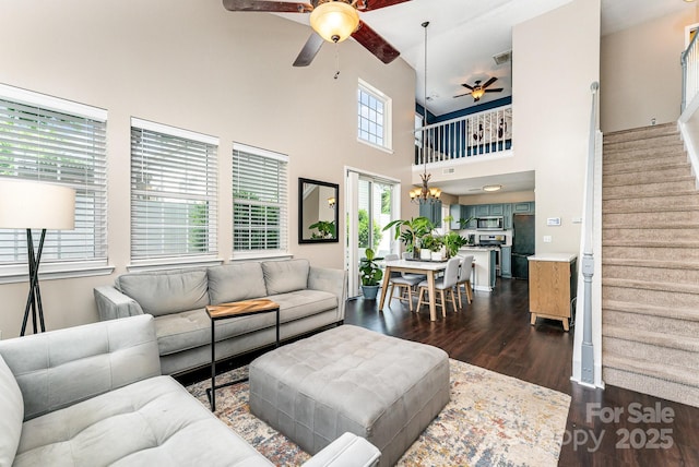 living area featuring dark wood finished floors, visible vents, a towering ceiling, ceiling fan, and stairs