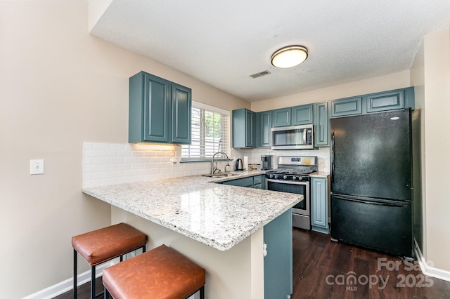 kitchen featuring a sink, a peninsula, backsplash, a kitchen bar, and appliances with stainless steel finishes