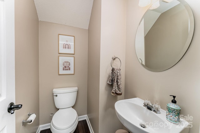 bathroom with a sink, toilet, wood finished floors, a textured ceiling, and baseboards