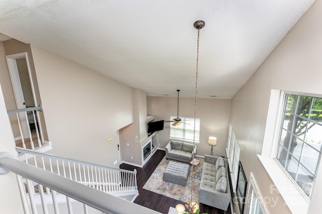 living room featuring wood finished floors, a fireplace, a textured ceiling, baseboards, and ceiling fan